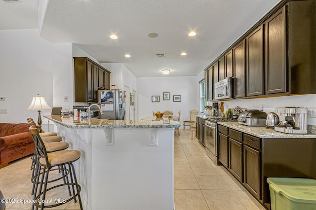 kitchen featuring light stone counters, light tile patterned floors, dark brown cabinetry, and appliances with stainless steel finishes