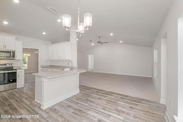 kitchen featuring stainless steel appliances, lofted ceiling, open floor plan, white cabinetry, and a sink