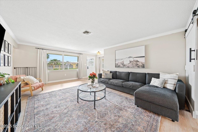 living area with a barn door, visible vents, ornamental molding, a textured ceiling, and light wood-type flooring