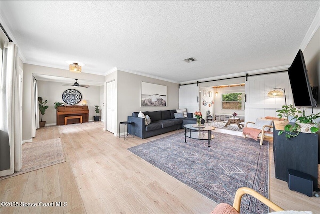 living area featuring a barn door, a fireplace, wood finished floors, visible vents, and crown molding