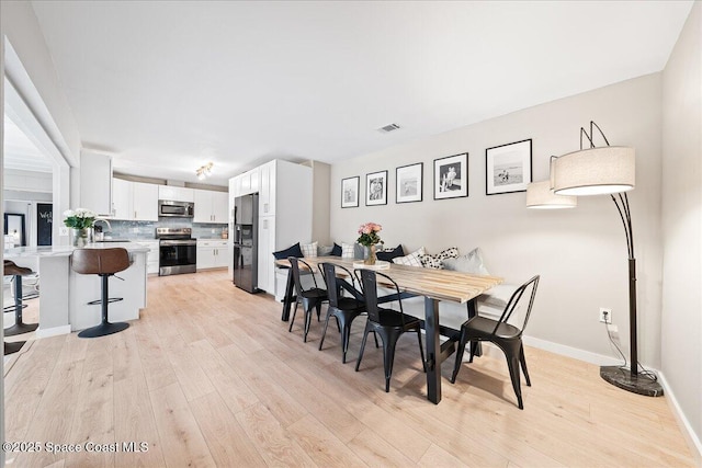 dining area with light wood-style flooring, visible vents, and baseboards