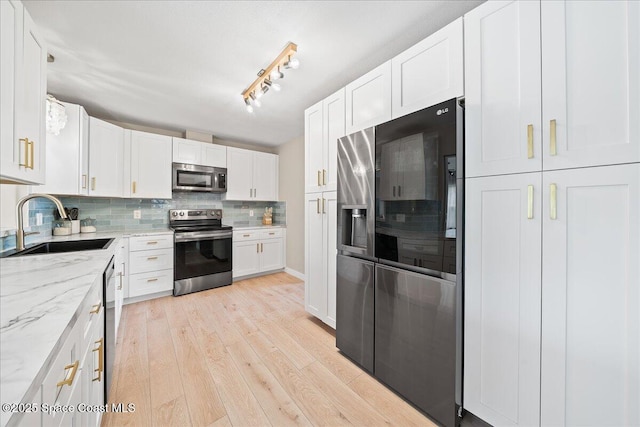 kitchen with tasteful backsplash, white cabinets, appliances with stainless steel finishes, light wood-type flooring, and a sink