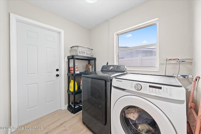 washroom featuring laundry area, washing machine and dryer, a textured ceiling, and light wood-style floors