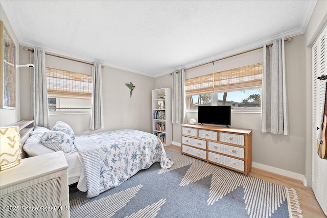 bedroom featuring a textured ceiling, baseboards, wood finished floors, and crown molding