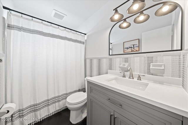 full bathroom featuring a wainscoted wall, tile walls, visible vents, toilet, and vanity