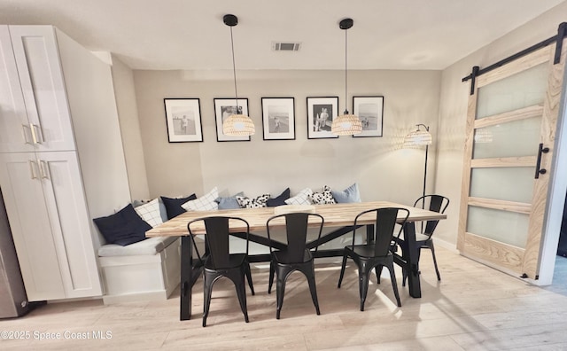 dining area with light wood finished floors, a barn door, breakfast area, and visible vents