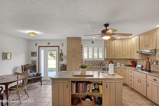 kitchen with sink, tasteful backsplash, black electric stovetop, a healthy amount of sunlight, and a kitchen island with sink