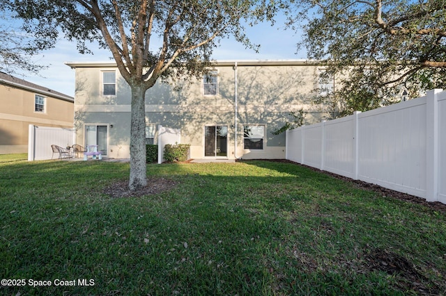 rear view of house featuring a yard, a fenced backyard, and stucco siding