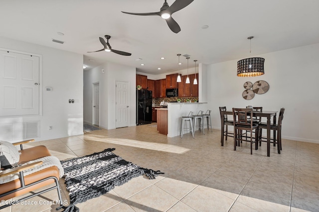 living area with light tile patterned flooring, ceiling fan, visible vents, and baseboards