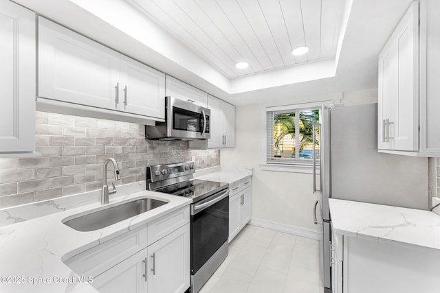 kitchen with appliances with stainless steel finishes, white cabinetry, sink, a tray ceiling, and light stone countertops