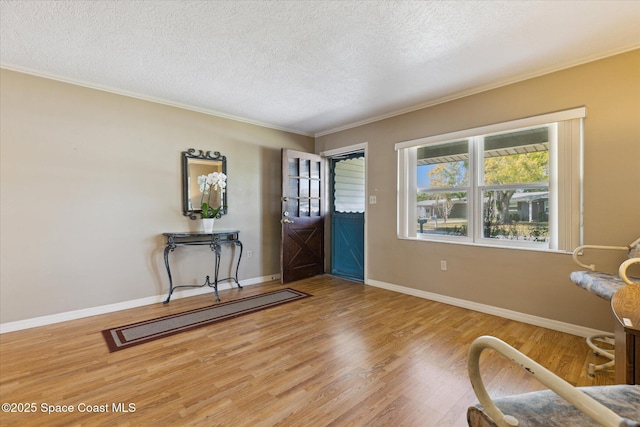 entryway with crown molding, a textured ceiling, baseboards, and wood finished floors