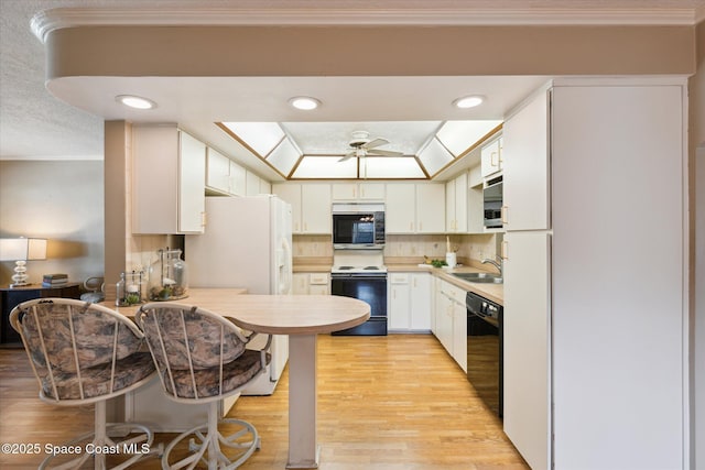 kitchen with black dishwasher, electric range oven, stainless steel microwave, white cabinetry, and a sink