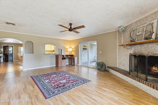 living room with a warm lit fireplace, a textured ceiling, visible vents, and wood finished floors