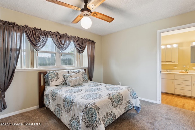 carpeted bedroom with a sink, a textured ceiling, ensuite bath, ceiling fan, and baseboards