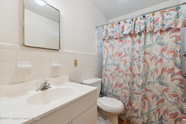 full bathroom featuring wainscoting, toilet, a shower with curtain, vanity, and tile walls