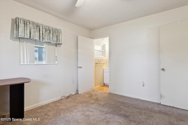 unfurnished bedroom featuring a textured ceiling, baseboards, ensuite bath, and light colored carpet