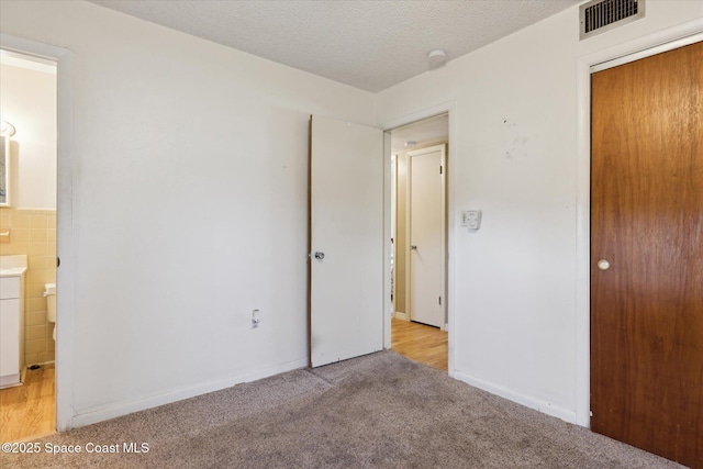 unfurnished bedroom featuring light carpet, visible vents, ensuite bathroom, a textured ceiling, and a closet