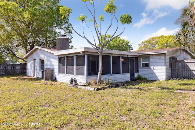 rear view of house featuring a sunroom, fence, a chimney, and a lawn