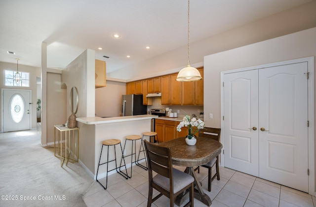 kitchen with stainless steel refrigerator, a breakfast bar, light tile patterned flooring, decorative light fixtures, and kitchen peninsula