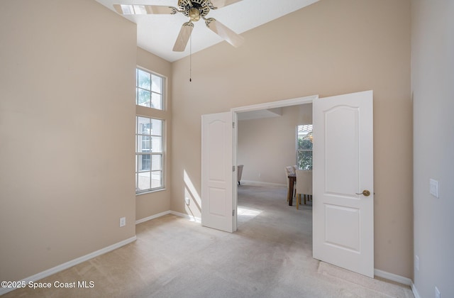 unfurnished room featuring a high ceiling, light colored carpet, and ceiling fan