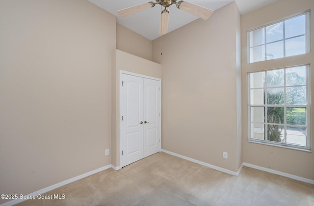 carpeted spare room featuring ceiling fan and a towering ceiling