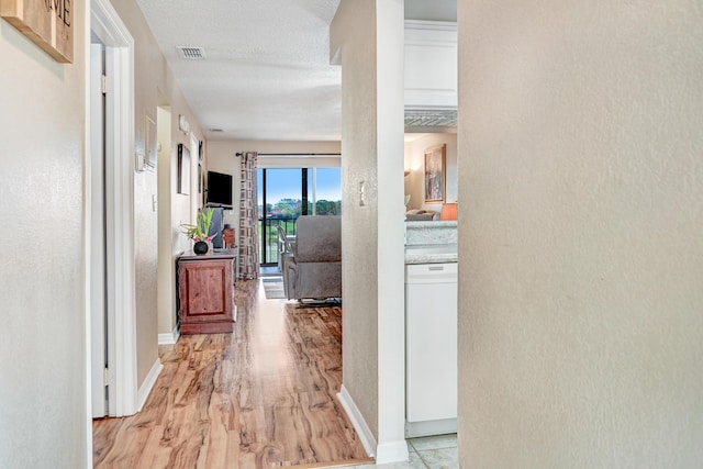 hallway with a textured ceiling and light hardwood / wood-style flooring