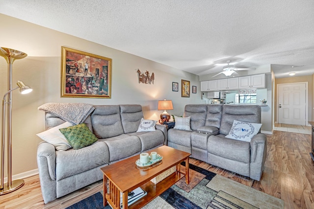 living room featuring ceiling fan, a textured ceiling, and light wood-type flooring