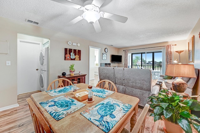 dining space with ceiling fan, light hardwood / wood-style flooring, a textured ceiling, and stacked washing maching and dryer