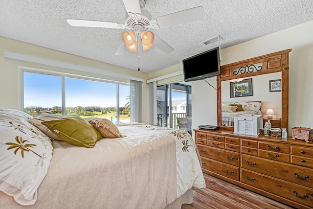 bedroom featuring ceiling fan, a textured ceiling, light hardwood / wood-style flooring, and access to outside