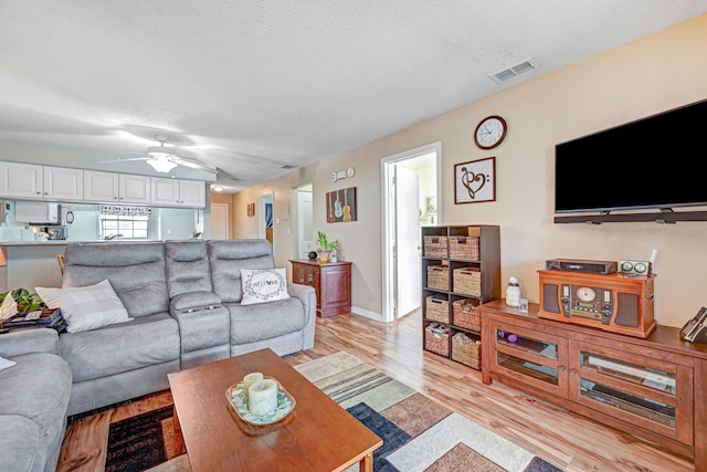 living room with ceiling fan, a textured ceiling, and light wood-type flooring