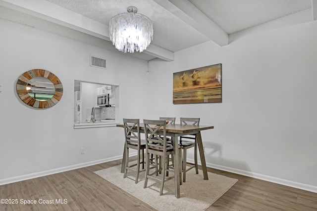 dining room with an inviting chandelier, hardwood / wood-style floors, a textured ceiling, and beamed ceiling