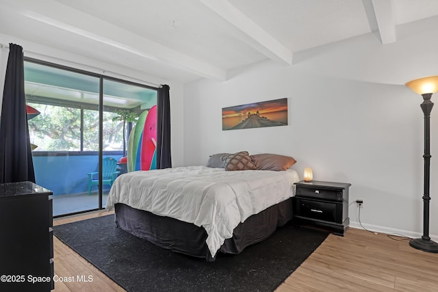 bedroom with hardwood / wood-style floors, beam ceiling, and access to outside