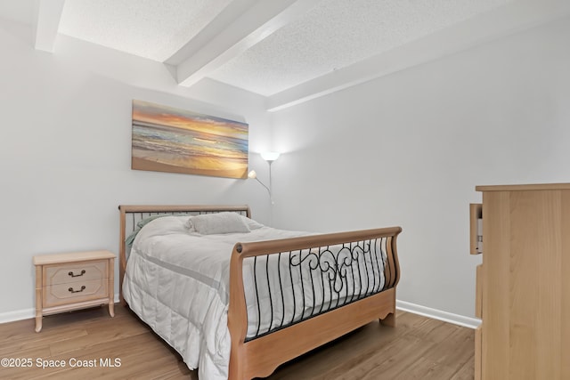 bedroom with beamed ceiling, a textured ceiling, and hardwood / wood-style flooring