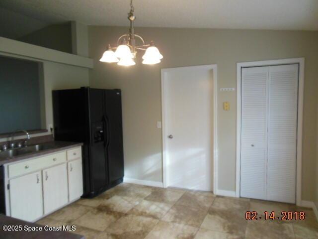 kitchen with lofted ceiling, sink, white cabinetry, hanging light fixtures, and black fridge