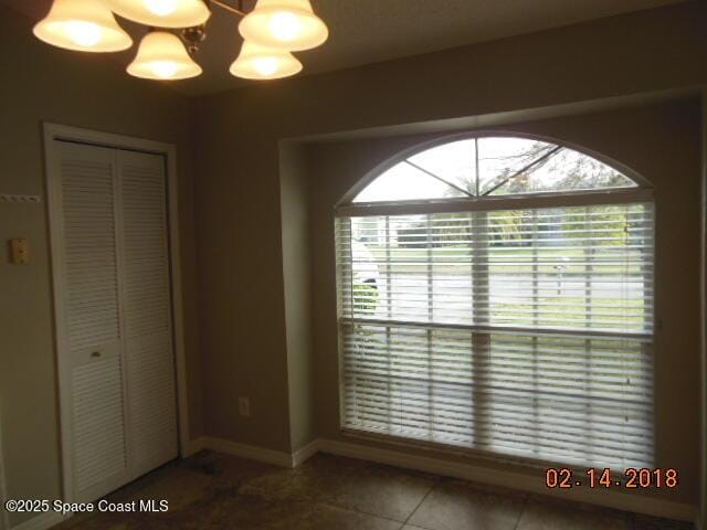 interior space featuring multiple windows, a notable chandelier, dark tile patterned flooring, and a closet