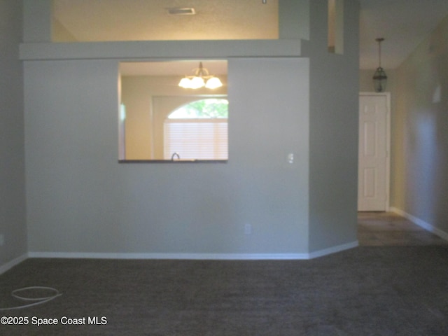 unfurnished room featuring an inviting chandelier and dark carpet