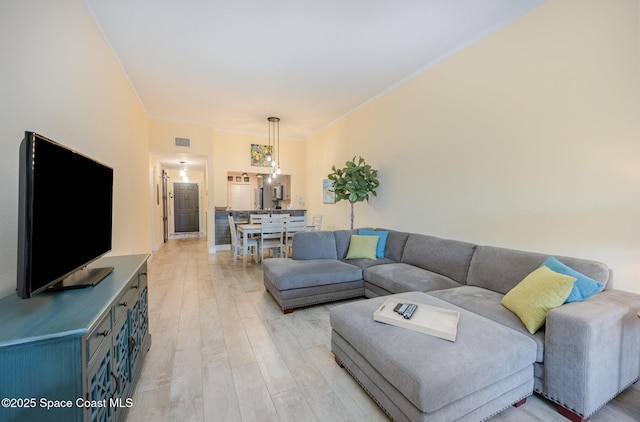 living area featuring light wood finished floors, visible vents, and ornamental molding