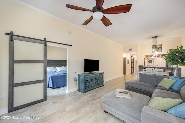 living area with a barn door, baseboards, a ceiling fan, light wood-style flooring, and washer and dryer