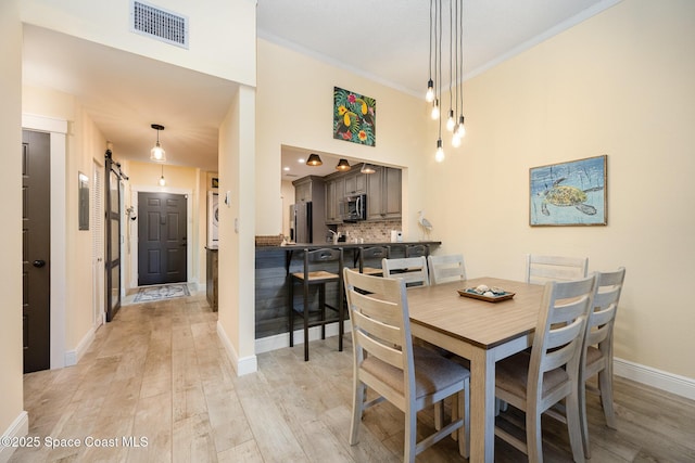 dining space featuring a high ceiling, visible vents, baseboards, ornamental molding, and light wood-type flooring