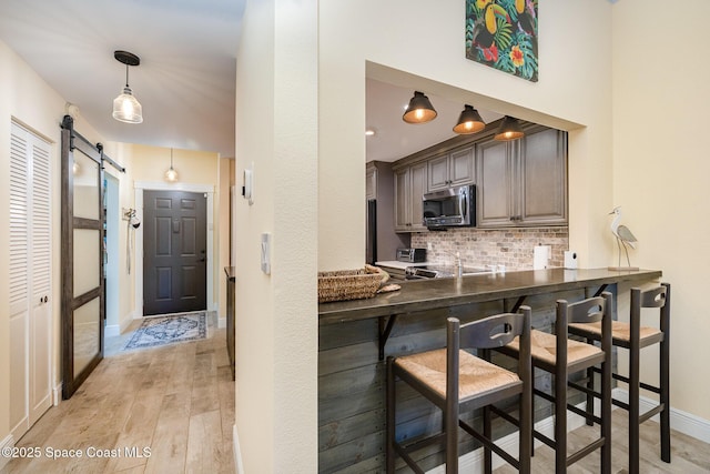 kitchen with a breakfast bar, stainless steel microwave, dark countertops, and a barn door