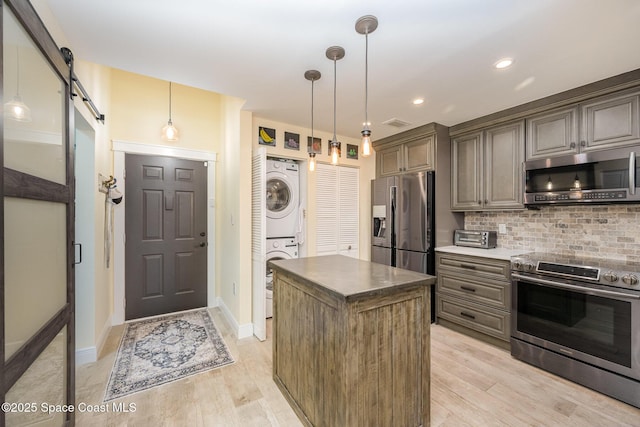 kitchen featuring a barn door, a kitchen island, stacked washer / drying machine, hanging light fixtures, and appliances with stainless steel finishes