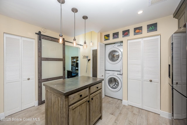 laundry area with laundry area, a barn door, visible vents, stacked washer / dryer, and light wood-style floors