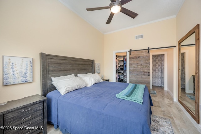 bedroom featuring a walk in closet, crown molding, light wood finished floors, visible vents, and a barn door