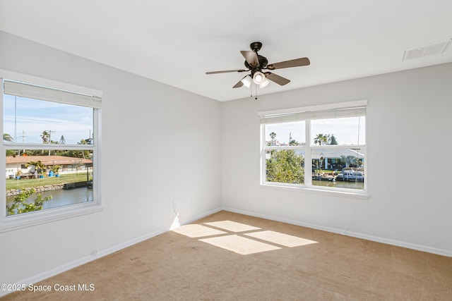 carpeted empty room with a water view, baseboards, visible vents, and ceiling fan