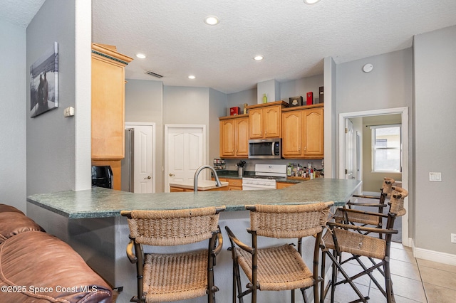 kitchen with a textured ceiling, light tile patterned floors, a kitchen breakfast bar, white range with gas cooktop, and kitchen peninsula