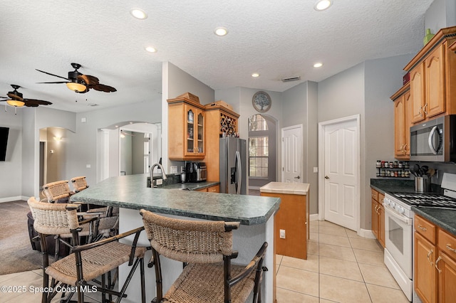 kitchen featuring light tile patterned flooring, a kitchen island, appliances with stainless steel finishes, a kitchen bar, and kitchen peninsula