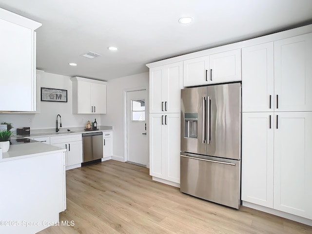 kitchen featuring appliances with stainless steel finishes, sink, white cabinets, and light wood-type flooring