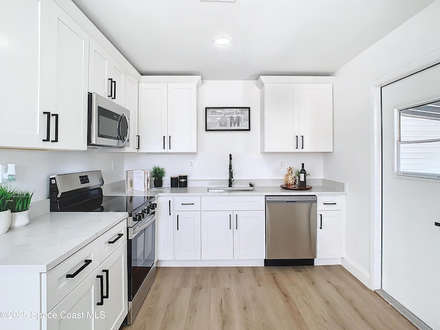 kitchen with sink, appliances with stainless steel finishes, light stone counters, light hardwood / wood-style floors, and white cabinets