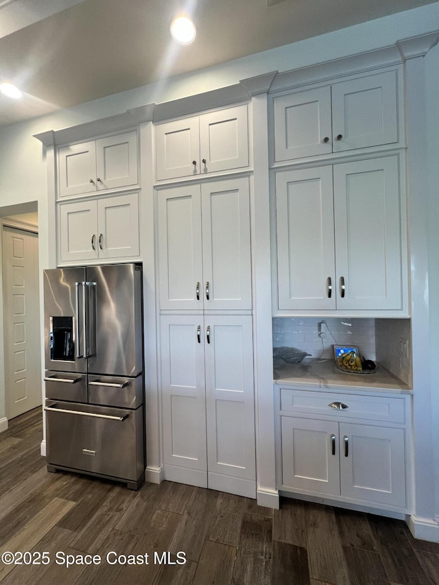kitchen with dark wood-type flooring, high end fridge, tasteful backsplash, and white cabinets