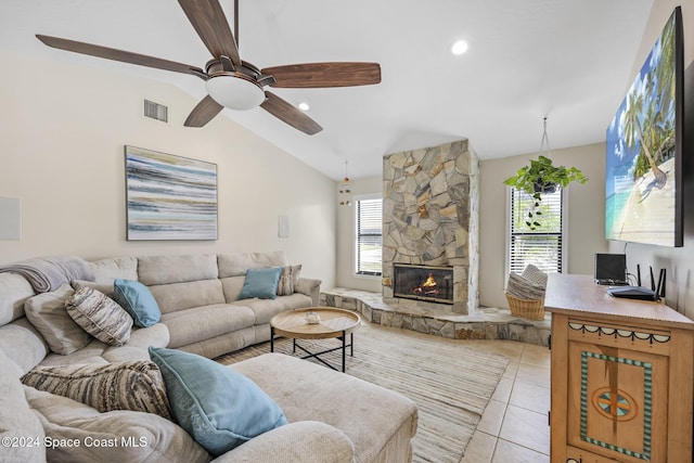 living room with a stone fireplace, a wealth of natural light, vaulted ceiling, and light tile patterned floors